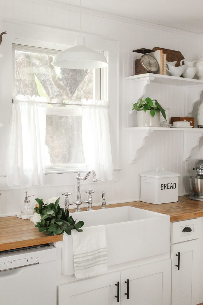 white single basin farmhouse apron sink with vintage chrome faucet and bread bin on butcher block countertop