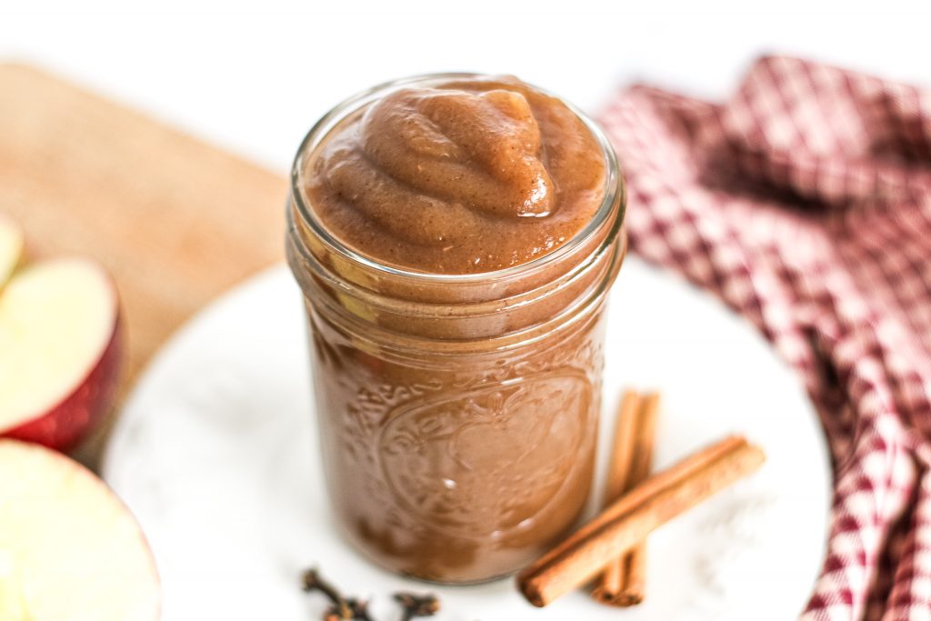 slow cooker apple butter in glass mason jar garnished with cloves and cinnamon sticks
