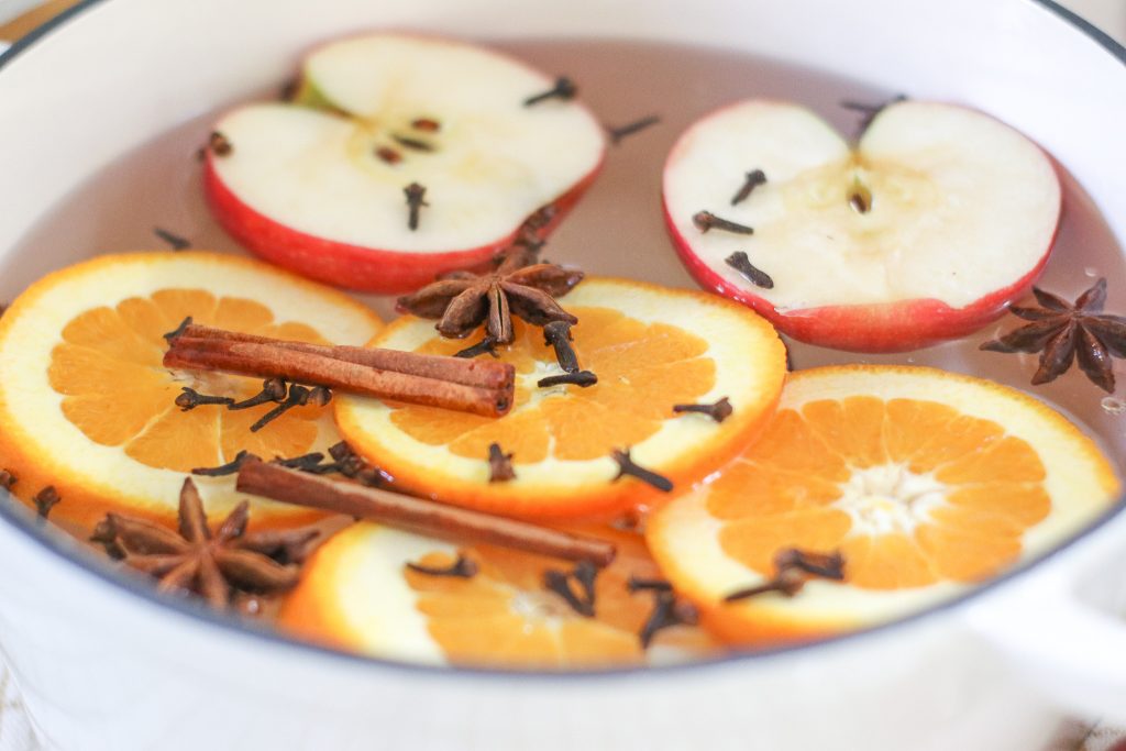 apples oranges star anise and cinnamon in water in white dutch oven for potpourri