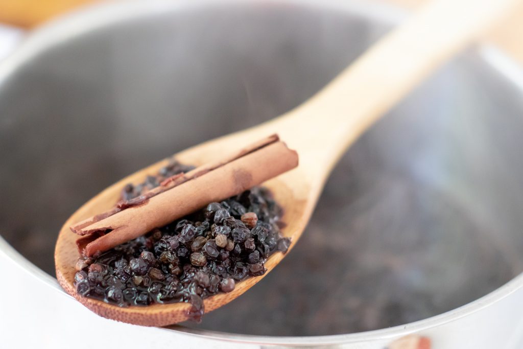 wooden spoon with cooked elderberries and cinnamon stick