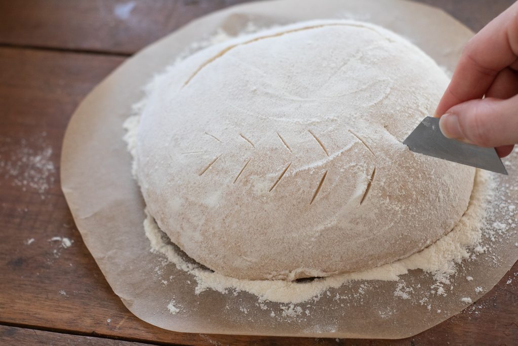 scoring bread dough with razorblades on parchment paper