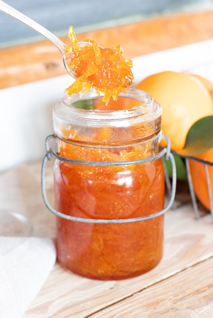 bright orange marmalade in vintage glass wire ball closure jar with stack of ranges behind 