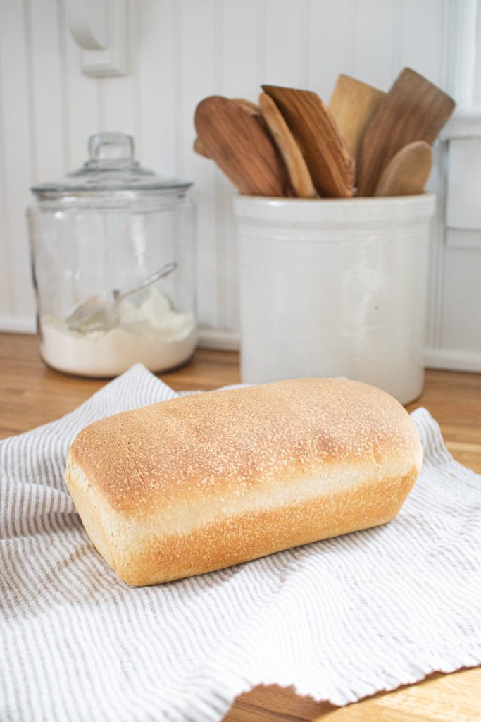 Golden sourdough country sandwich bread on cutting board with tea towel