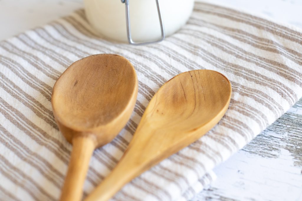 clean wooden utensils laying on a striped linen towel with wood butter sitting in background