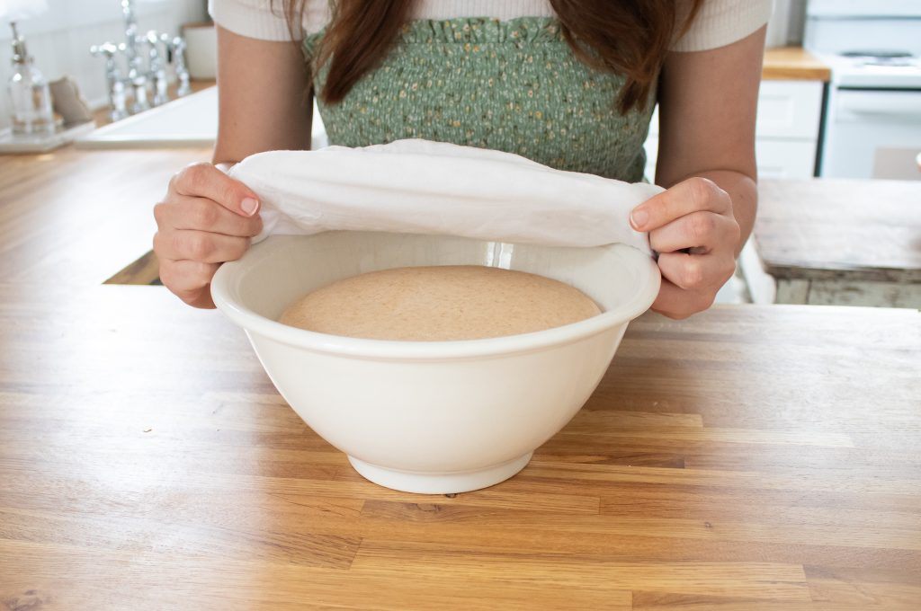 lady uncovering bagel dough in bowl