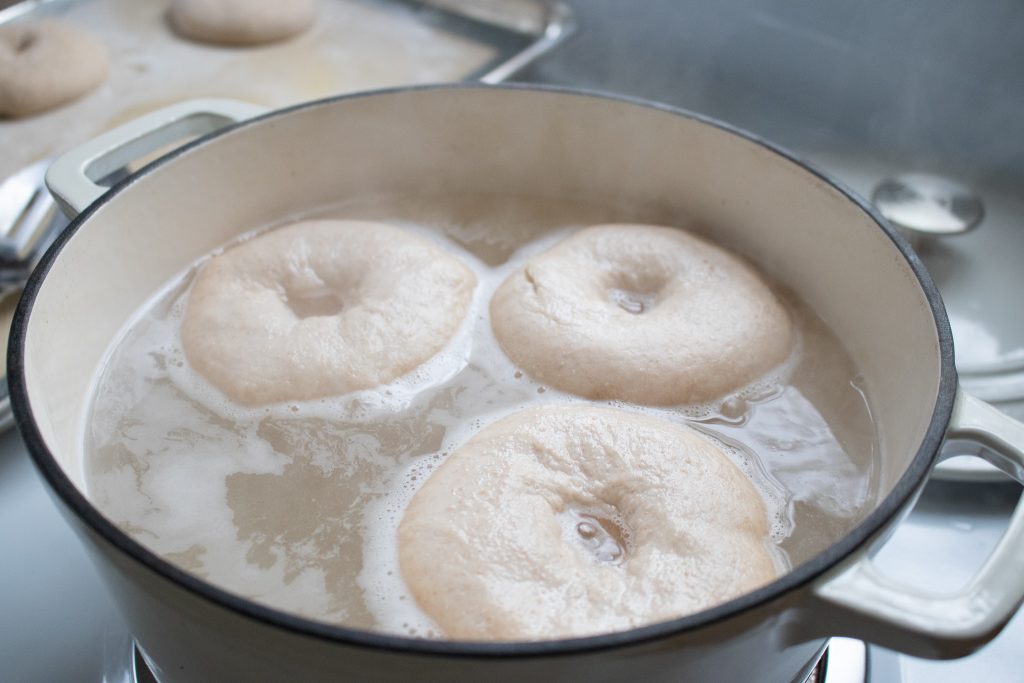 sourdough bagels boiling in an enamel pot of water