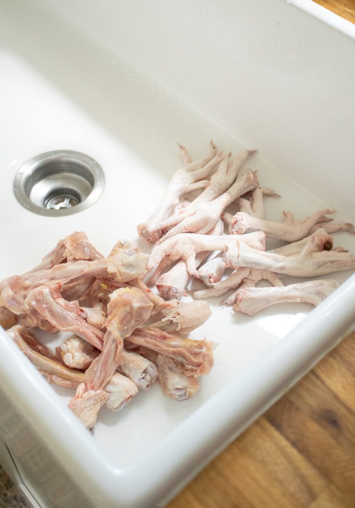 raw chicken feet and chicken bones sitting in a white farmhouse sink