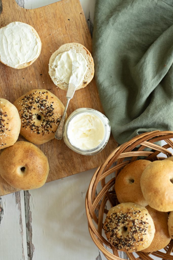 easy sourdough bagels bread on cutting board and in wicker basket with cream cheese contained sitting out