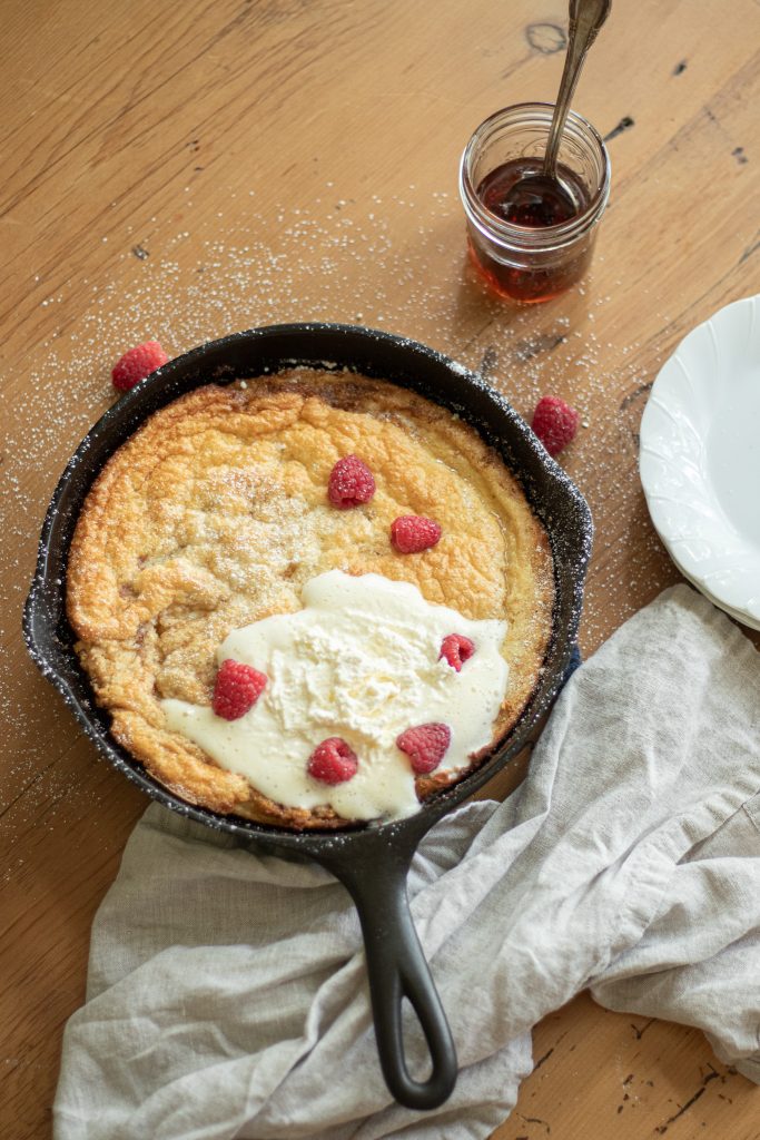 cast iron skillet with fluffy dutch baby sitting on kitchen table garnished with fresh berries