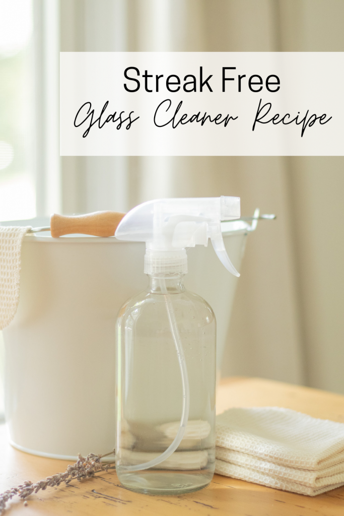 clear bottle of homemade glass cleaner sitting in front of white bucket 