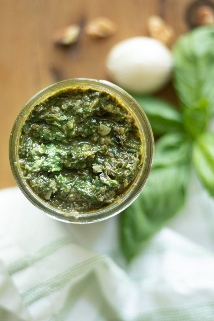 green fresh basil pesto in glass jar on wooden table